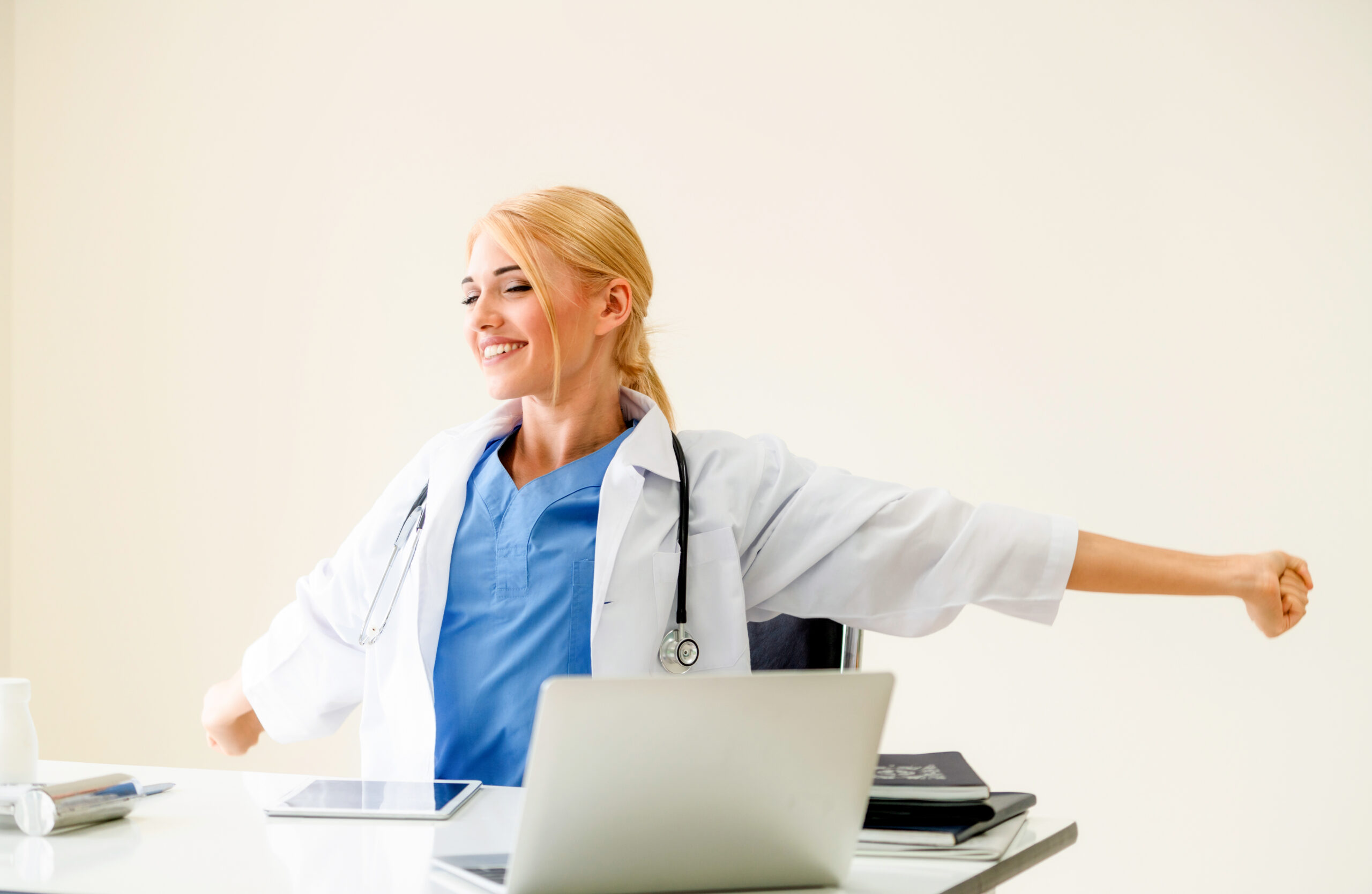 Relaxed woman doctor takes deep breath while working on medical report at office table. Stress relief and control concept.