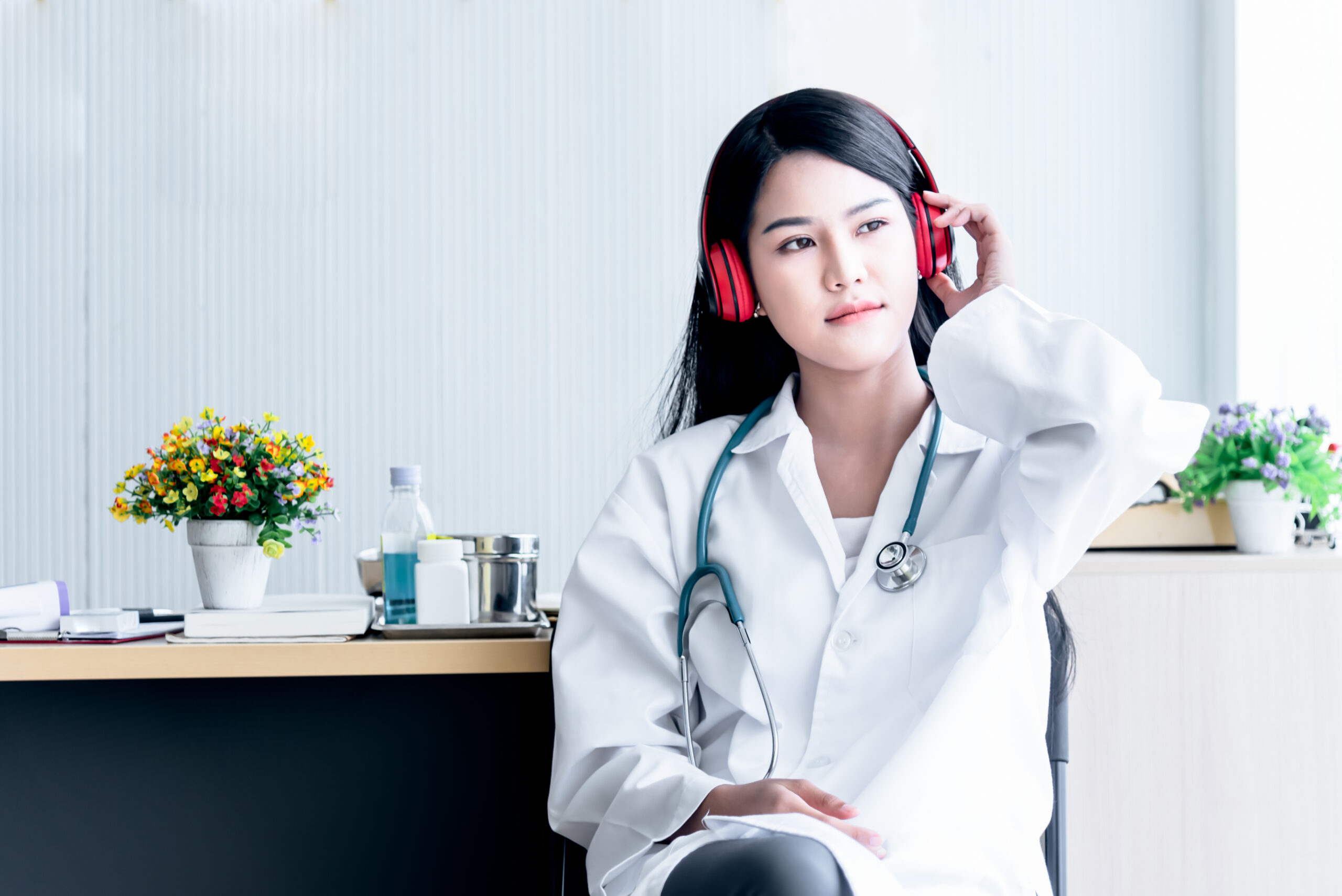 Asian female doctor Relaxing by listening to music from headphones While resting from the treatment of patients at the clinic with white background, to people and health care concept.